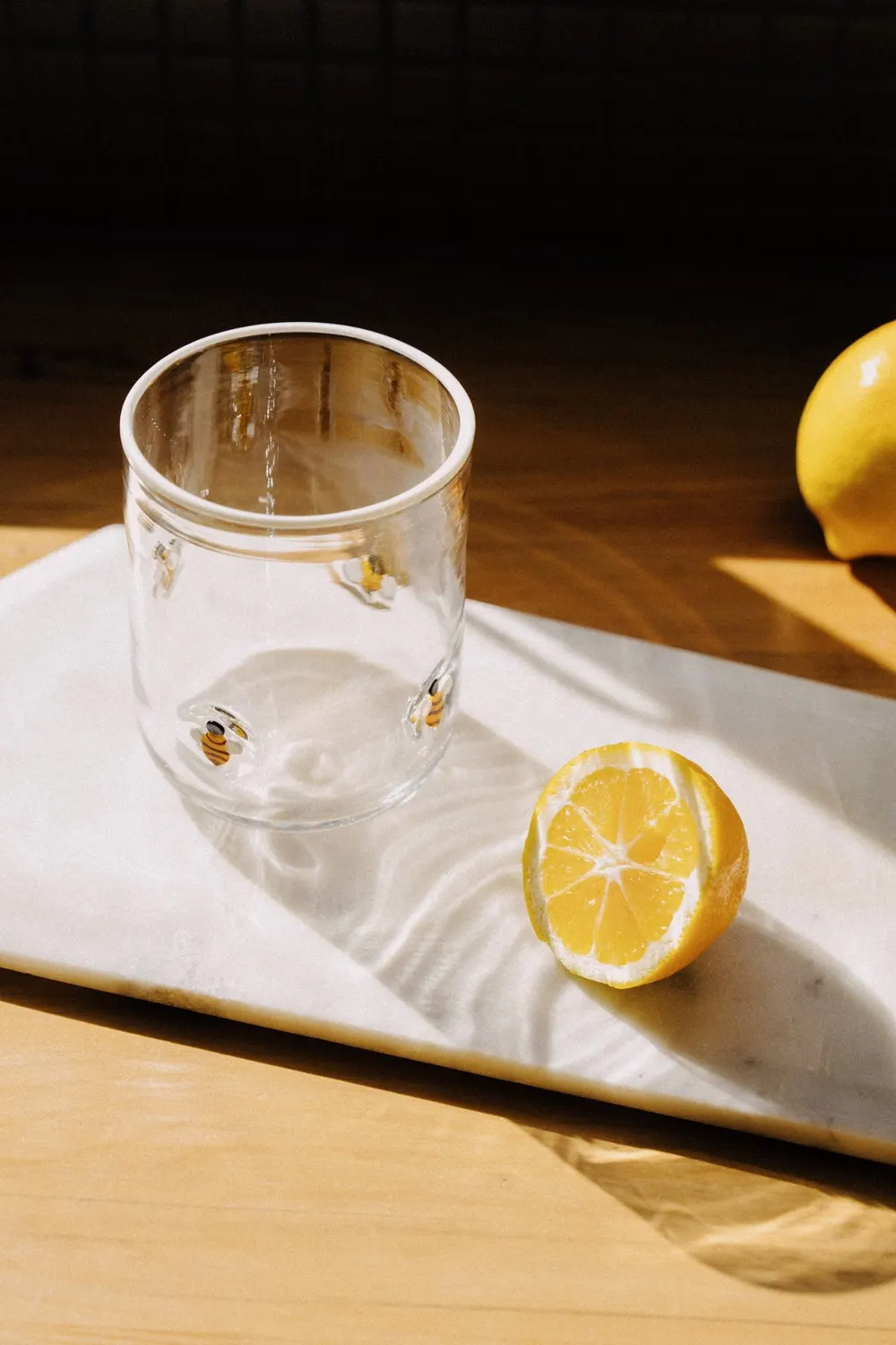 Bee Icon Cup on a marble board beside a halved lemon in sunlight