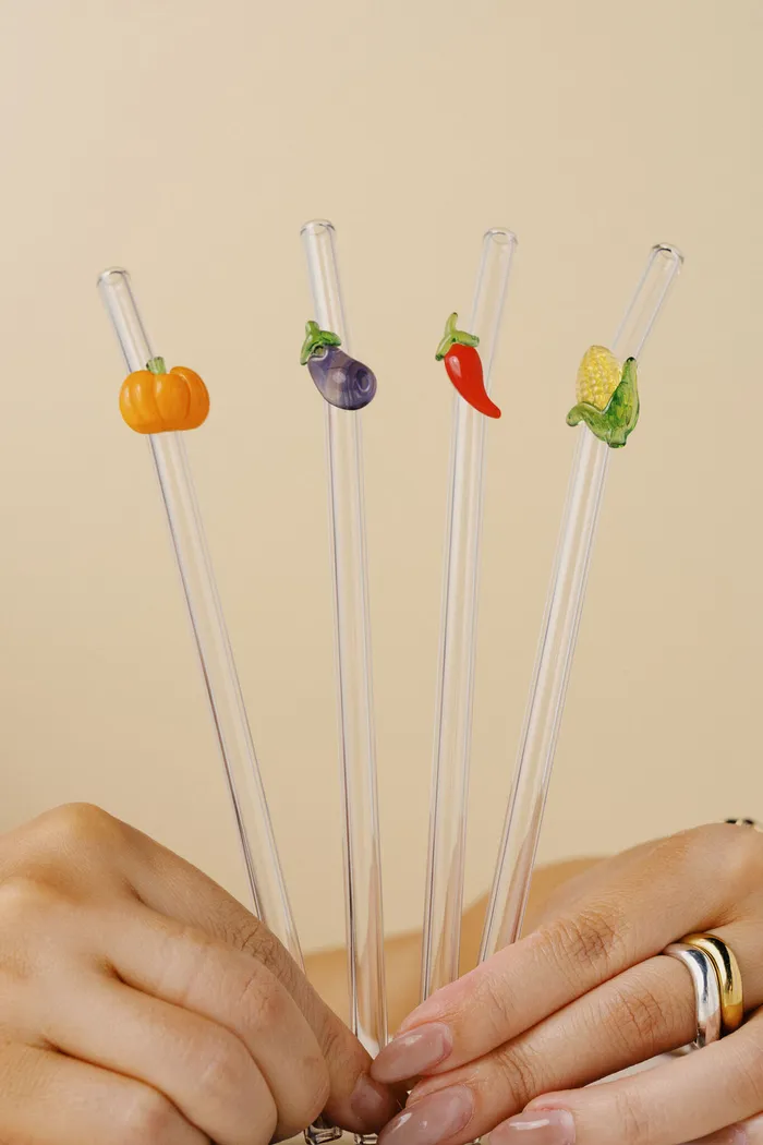 Hand holding the Vegetable Straw Set: glass straws with pumpkin, eggplant, chilli and corn charms