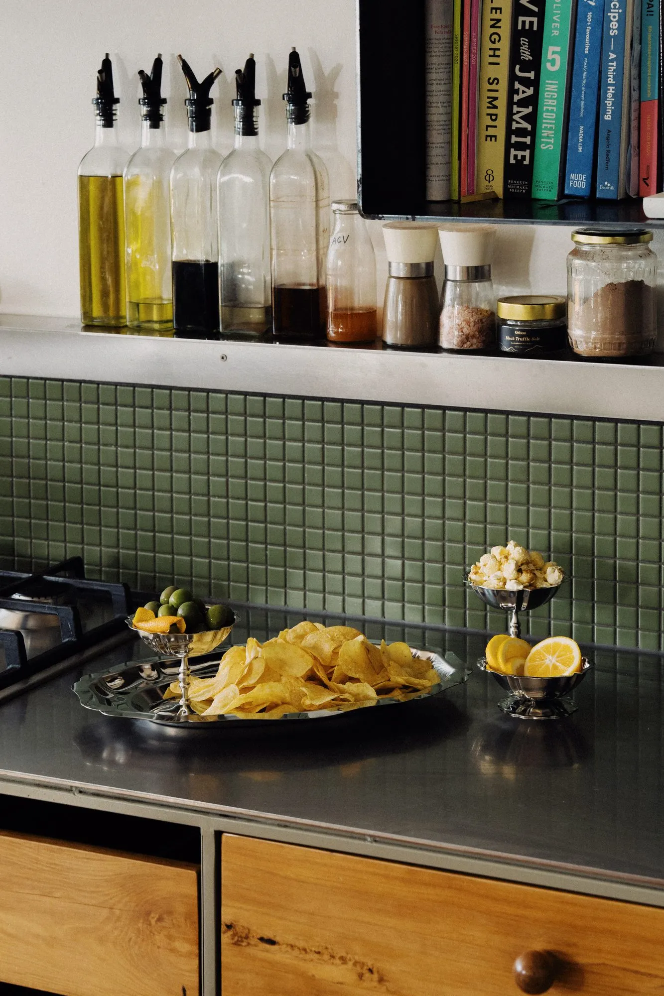 Riva stainless steel platter of potato chips beside coupes of olives, popcorn and lemon on a kitchen bench